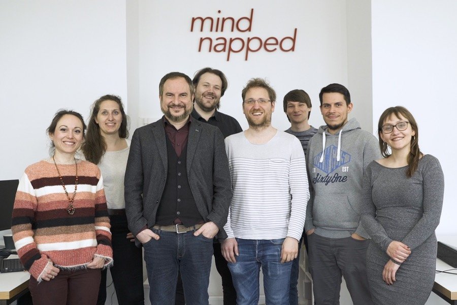 Das Team von mindnapped steht vor dem Logo an einer Wand